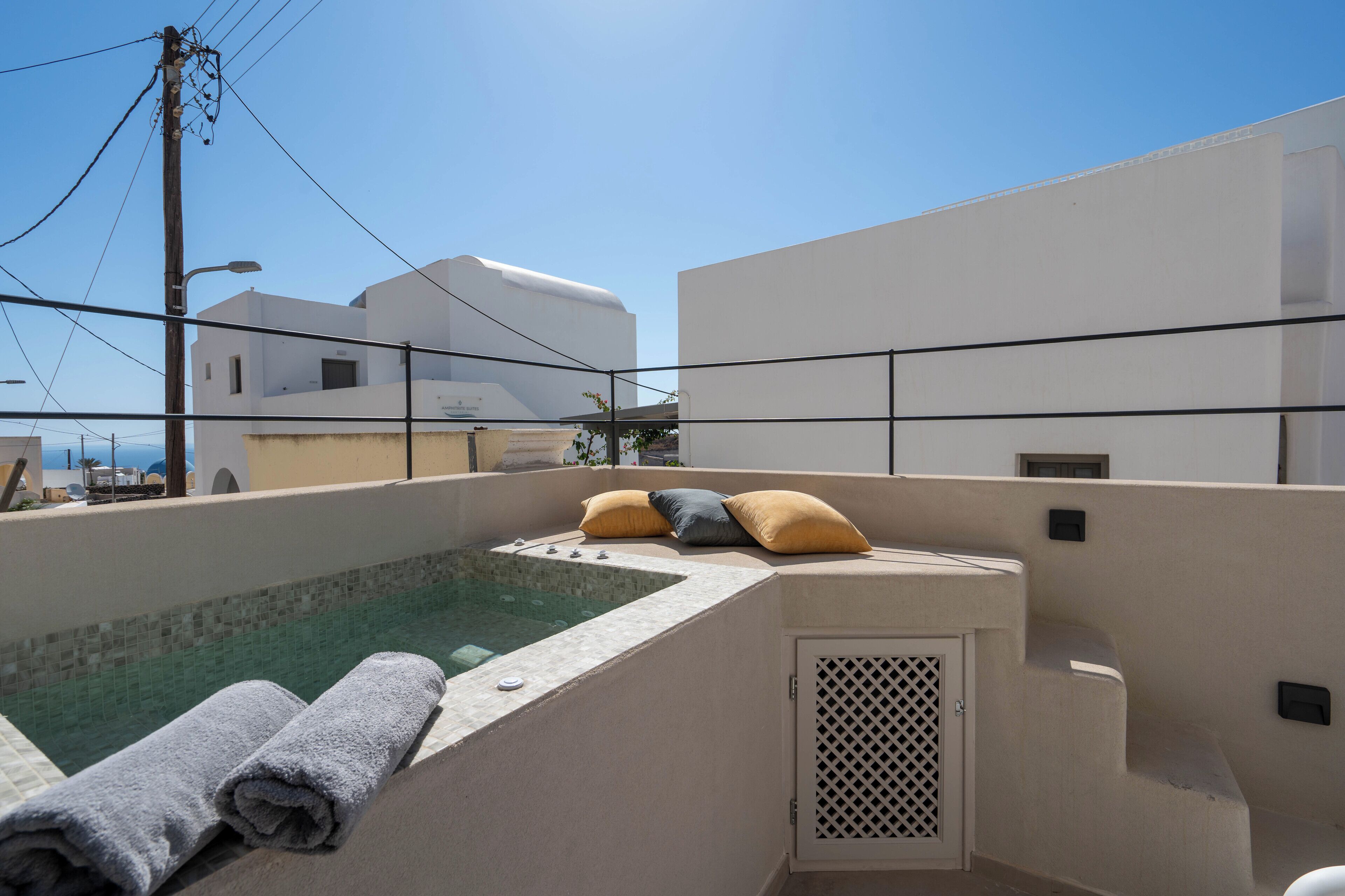 A rooftop pool area with a view of the sea, a white building, and a few pillows on the edge.