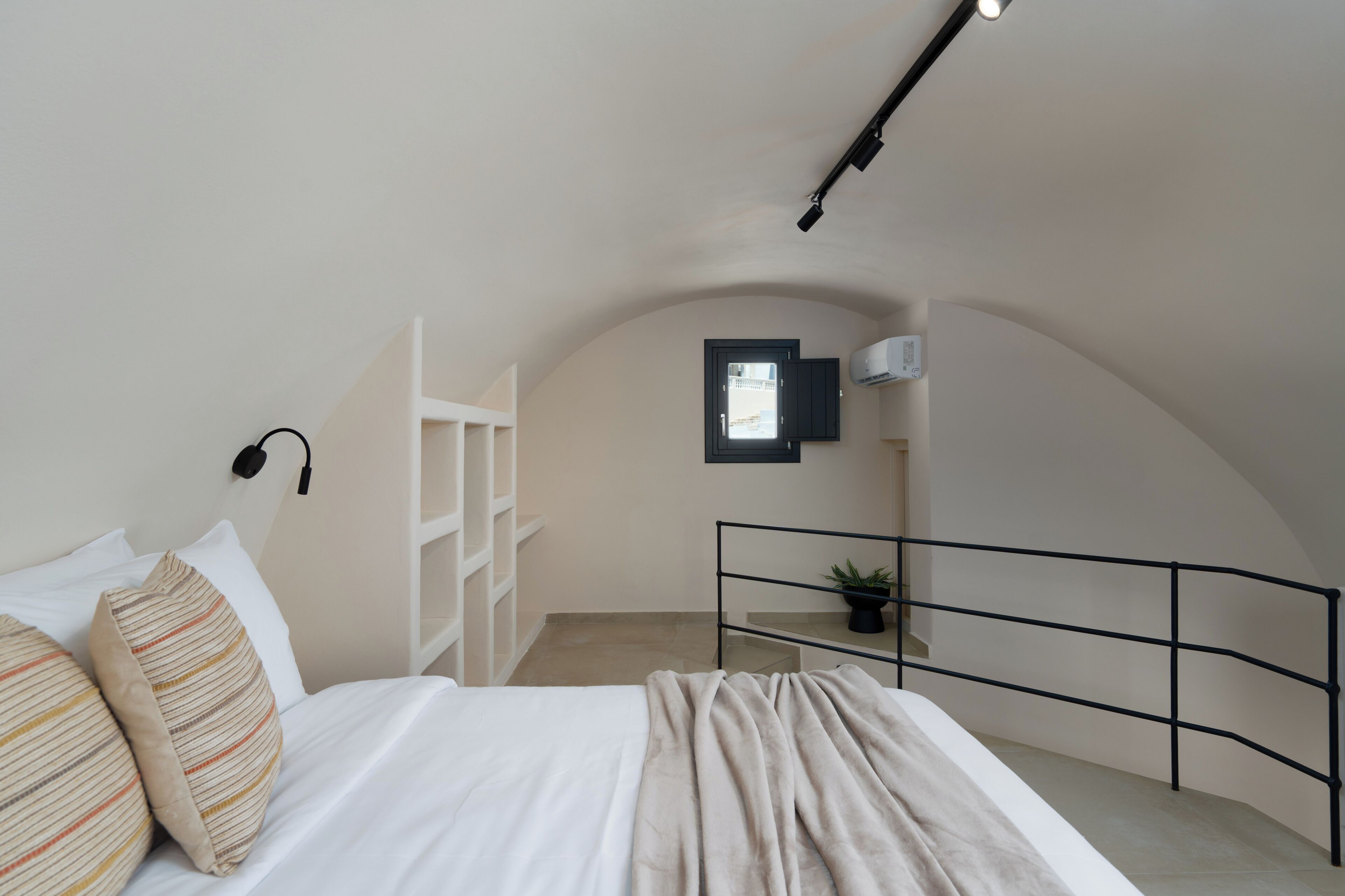 A bedroom with a bed, a window, a plant, and a ceiling light.