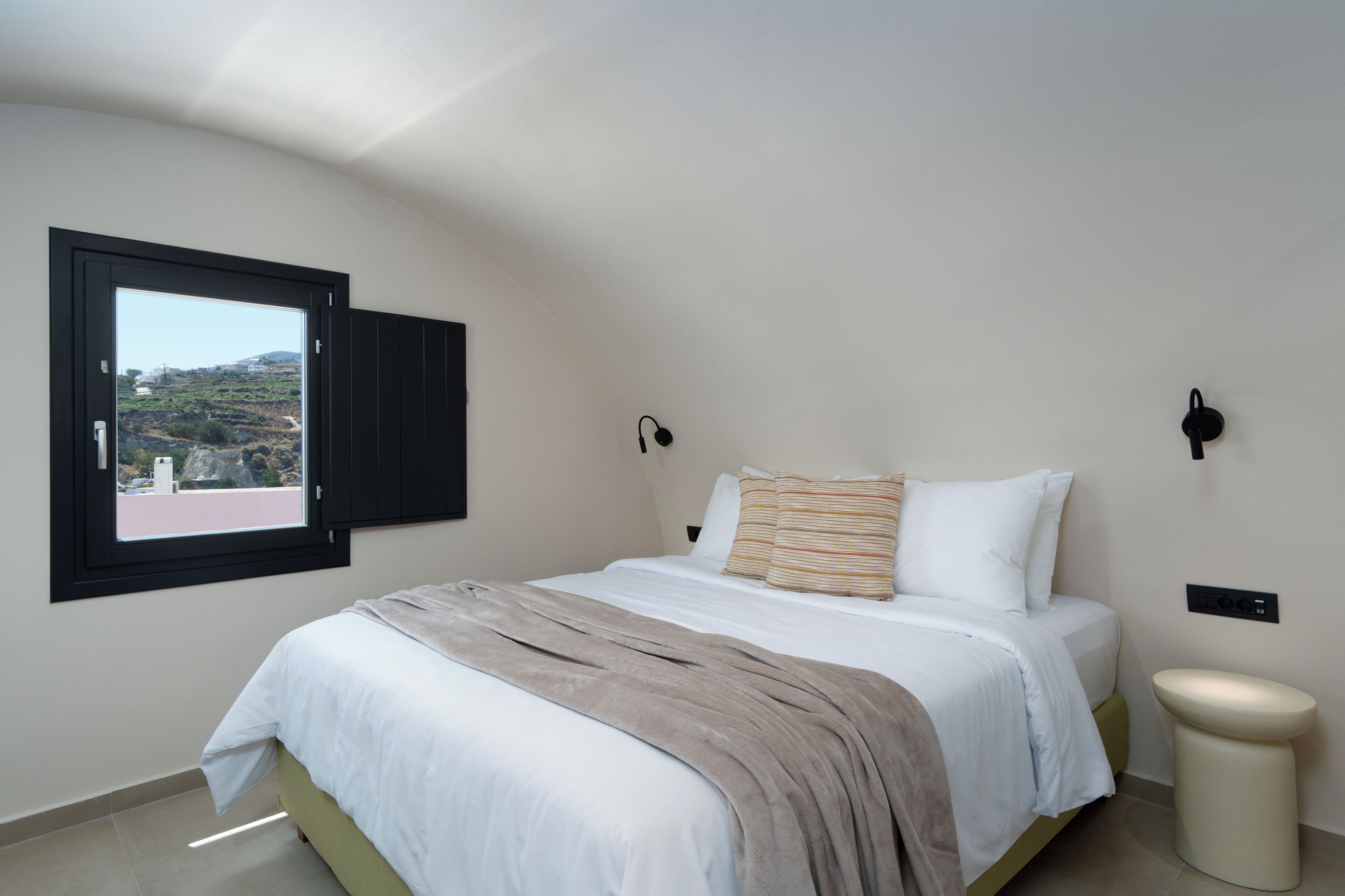 A bedroom with a bed, a window, a bedside table, and a wall-mounted light fixture.