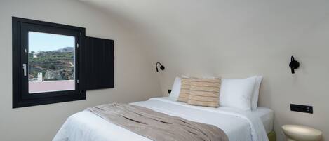 A bedroom with a bed, a window, a bedside table, and a wall-mounted light fixture.