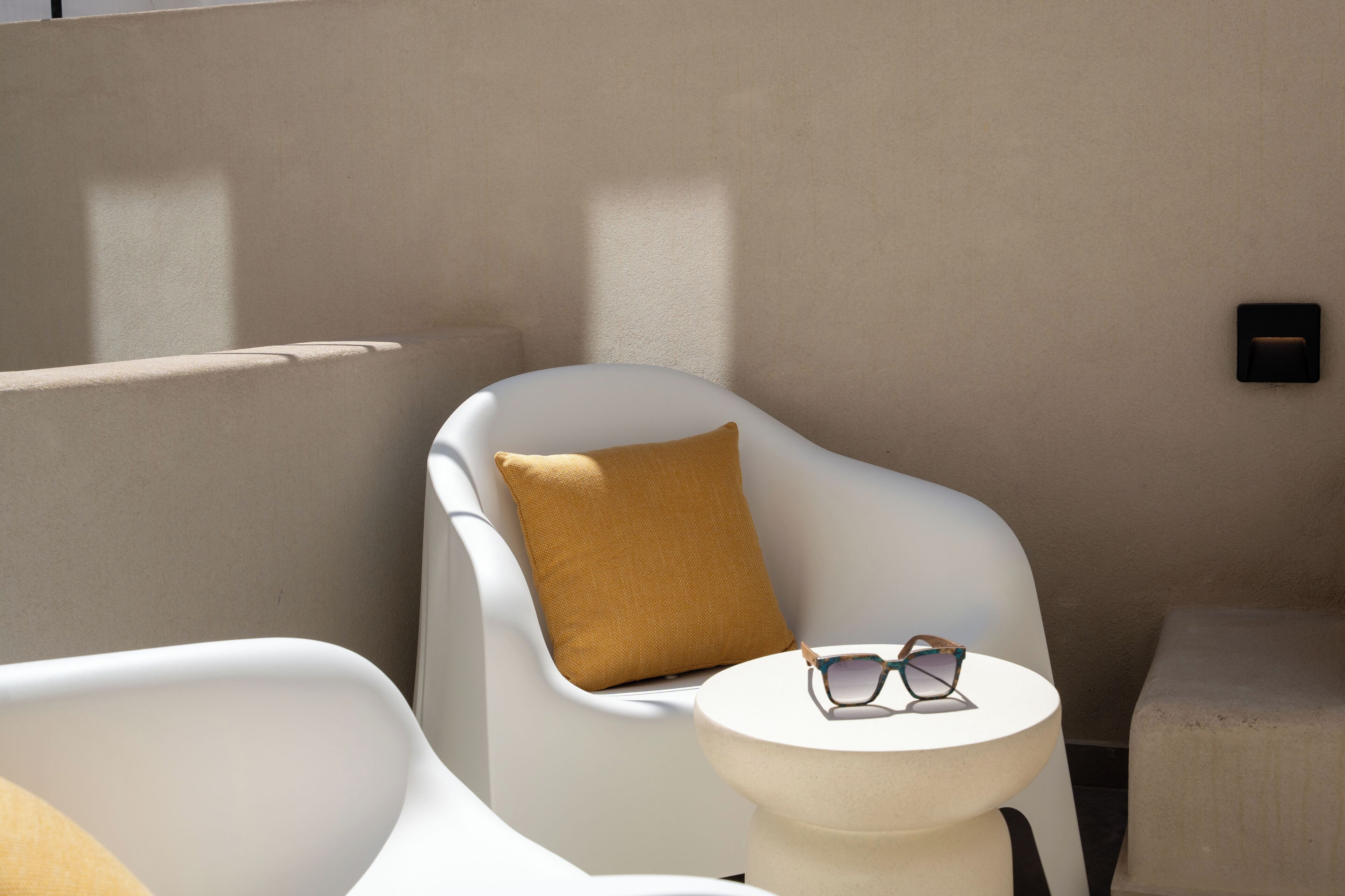 Una habitación moderna y minimalista con un sillón blanco, una mesa redonda y una almohada marrón.