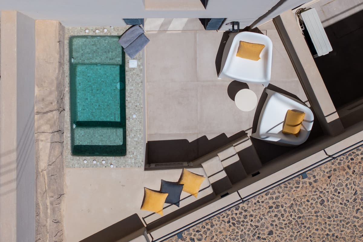 A top-down view of a pool area with a rectangular pool, a seating area with two chairs and a table, and a small round table with a single chair.