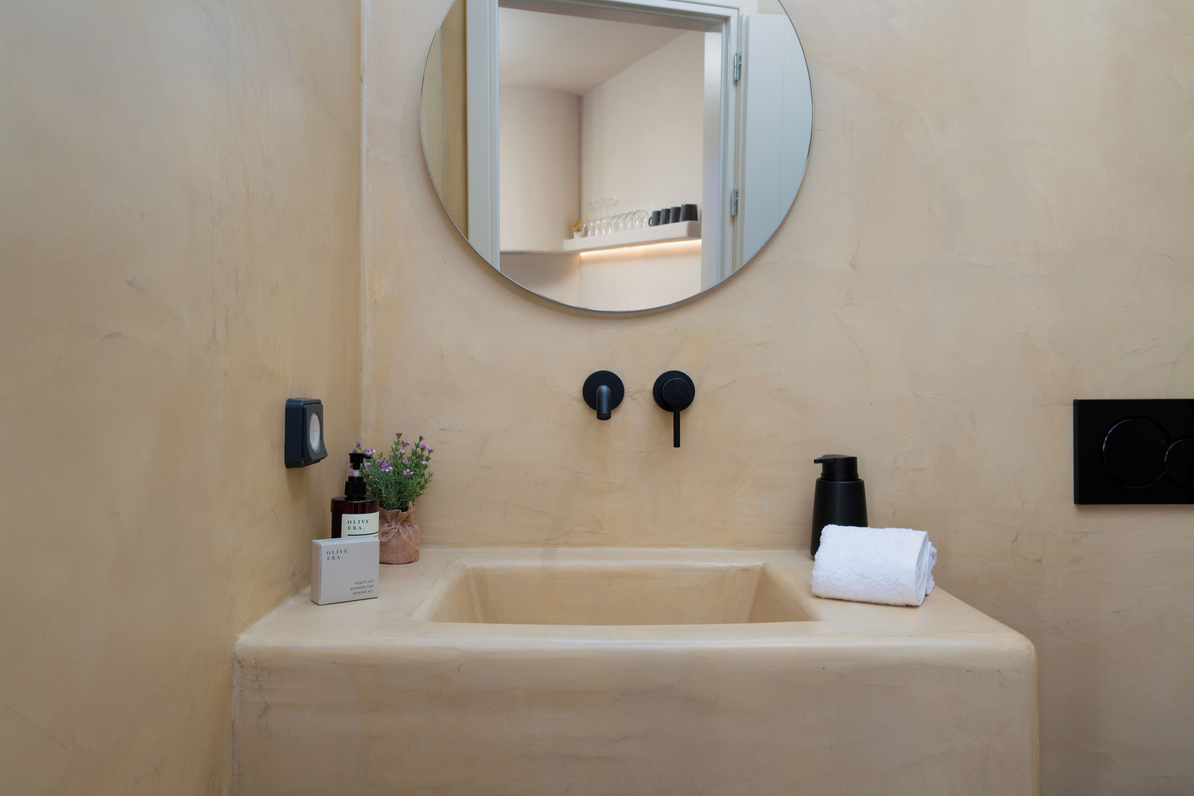 Une salle de bain avec un lavabo beige, un miroir, une serviette, un distributeur de savon et une petite plante en pot.