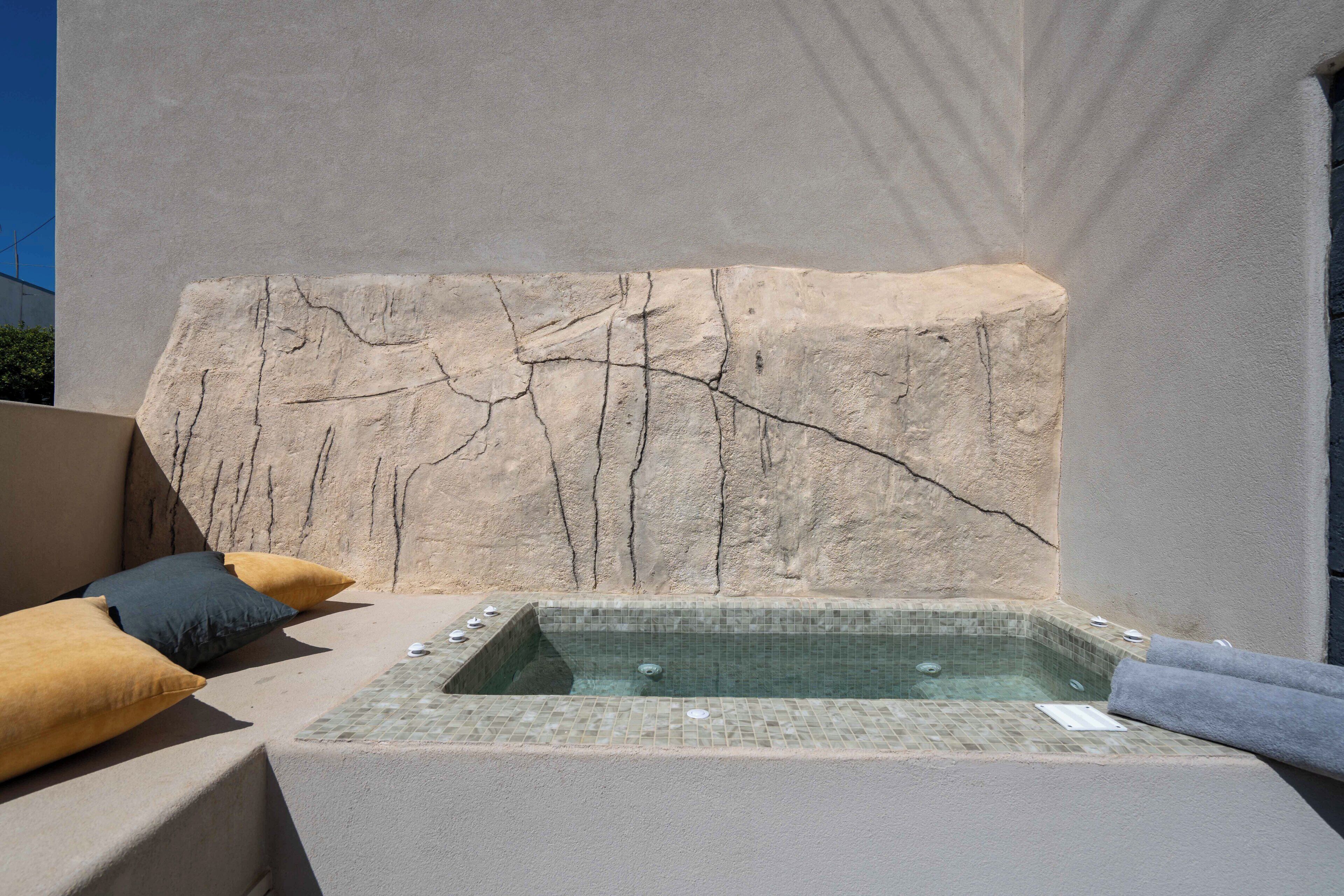 A spa area with a hot tub, a stone wall, and two pillows.