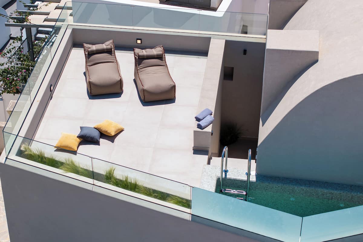A rooftop terrace with two lounge chairs, a small table, and a glass railing.