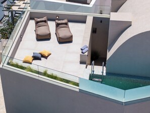Une terrasse sur le toit avec deux chaises longues, une petite table et une rambarde en verre.