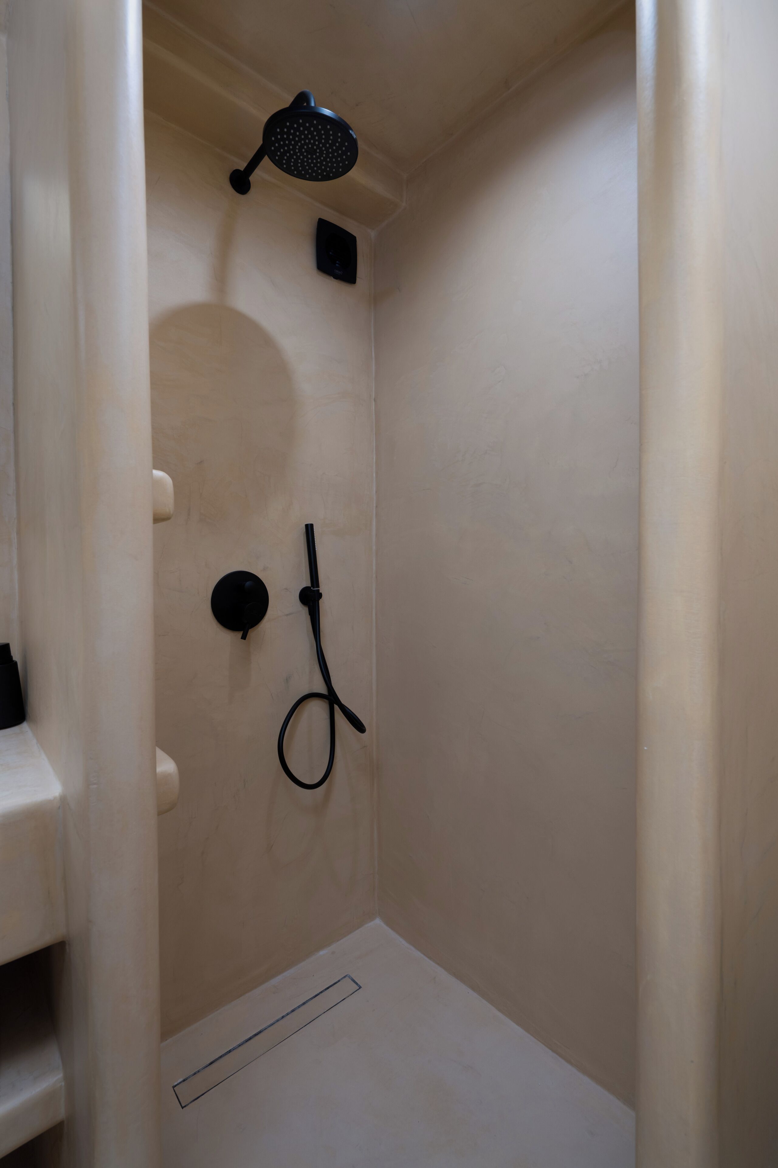 A small, enclosed shower area with a handheld showerhead and a wall-mounted control panel.