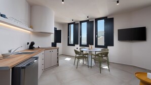 A modern kitchen with a wooden countertop, built-in dishwasher, and a dining area with a round table and wicker chairs. - White Orchid Apartments (Santorini)