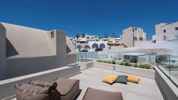 A rooftop terrace with a clear view of the cityscape, including buildings and a clear blue sky. - White Orchid Apartments (Santorini)