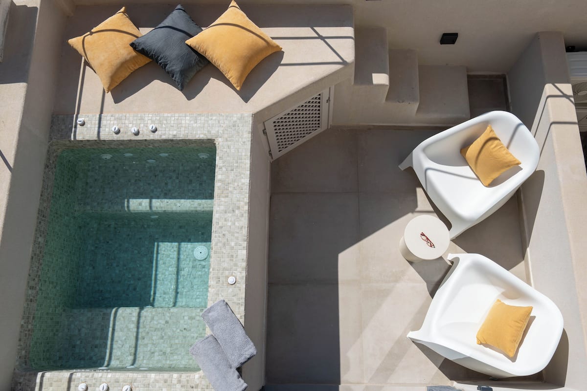 A rooftop pool area with a hot tub, two lounge chairs, and a small white table with a cushion.
