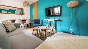 Una sala de estar moderna con una pared de acento color aguamarina, un televisor de pantalla plana, un sofá, una mesa de centro y un comedor con sillas.