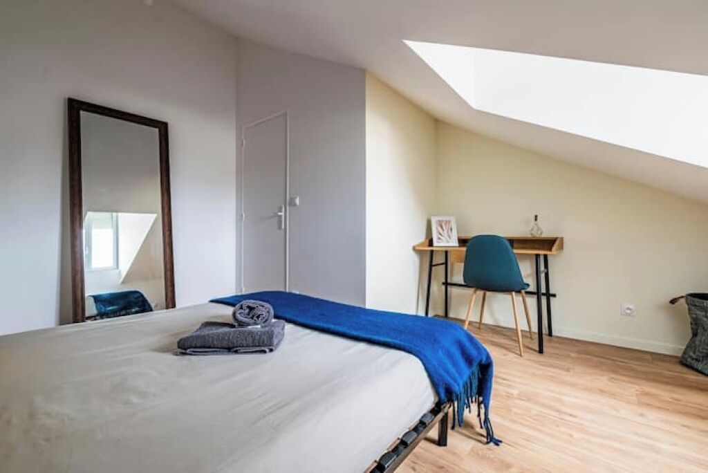 Quarto com cama, escrivaninha e cadeira. Há um claraboia sobre a cama.
