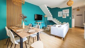 Un espacio habitable moderno con una pared de acento color aguamarina, un comedor con mesa de madera y sillas blancas, un sofá blanco y una escalera.
