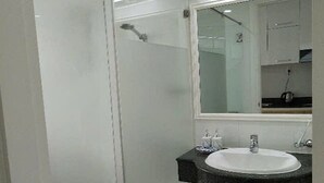 Un baño moderno con cabina de ducha de vidrio, un lavamanos blanco sobre encimera negra y un espejo sobre el lavamanos.