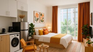 Una habitación de hotel moderna con cama, escritorio, lavadora y vistas a palmeras.