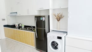 Una cocina moderna con armarios blancos, un refrigerador de acero inoxidable, una lavadora y una silla de madera.