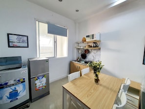 A compact kitchen with a refrigerator, microwave, and a small dining table with chairs. - Modern 1BR Near Airport – Kitchen, Washer, Quiet Stay (Hồ Chí Minh)