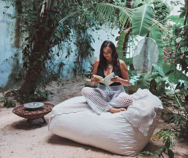 A person sitting on a bean bag chair reading a book in a garden with plants and a rustic wall.