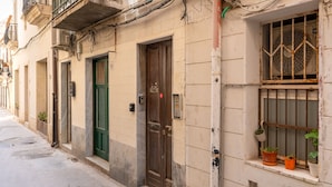 A narrow street with buildings featuring traditional architecture, including a wooden door and a window with barred security. - La Terrazza di Apollo (Syracuse)