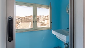 A bathroom with a window, a sink, and a view of buildings outside. - La Terrazza di Apollo (Syracuse)