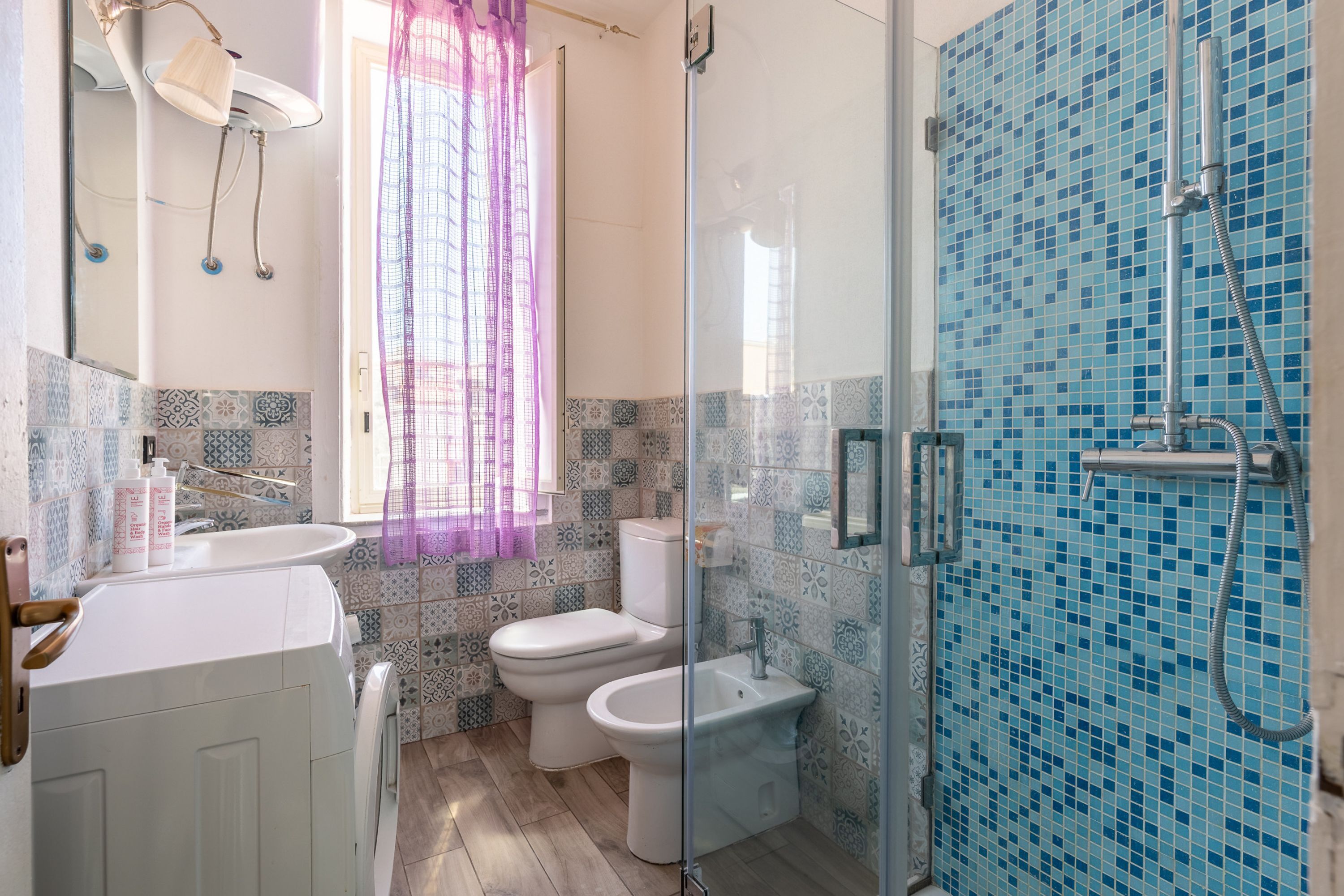 A bathroom with a shower, two toilets, a sink, and patterned tiles.