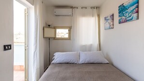 A bedroom with a bed, a window, an air conditioning unit, and two paintings on the wall. - La Terrazza di Apollo (Syracuse)