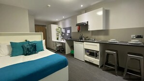 Ein modernes Hotelzimmer mit Bett, Schreibtisch, einer Küchenzeile und einer kleinen Bar.