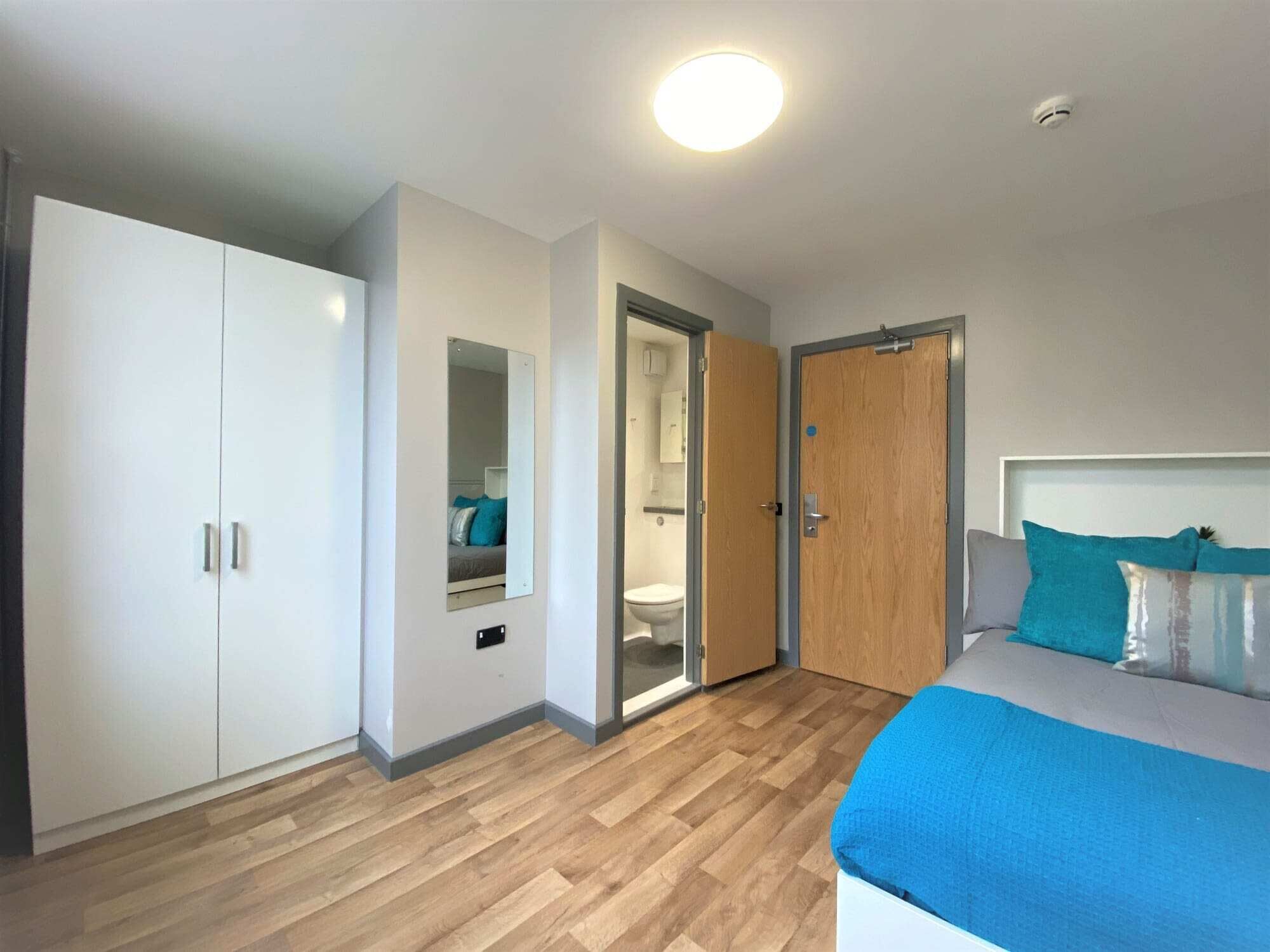 A bedroom with a bed, a wardrobe, a mirror, and a door leading to a bathroom.