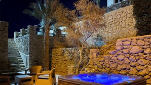 A hot tub with a wooden exterior, surrounded by stone walls and a wooden deck.