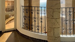 A balcony with stone columns and a wrought iron railing, overlooking a cityscape.