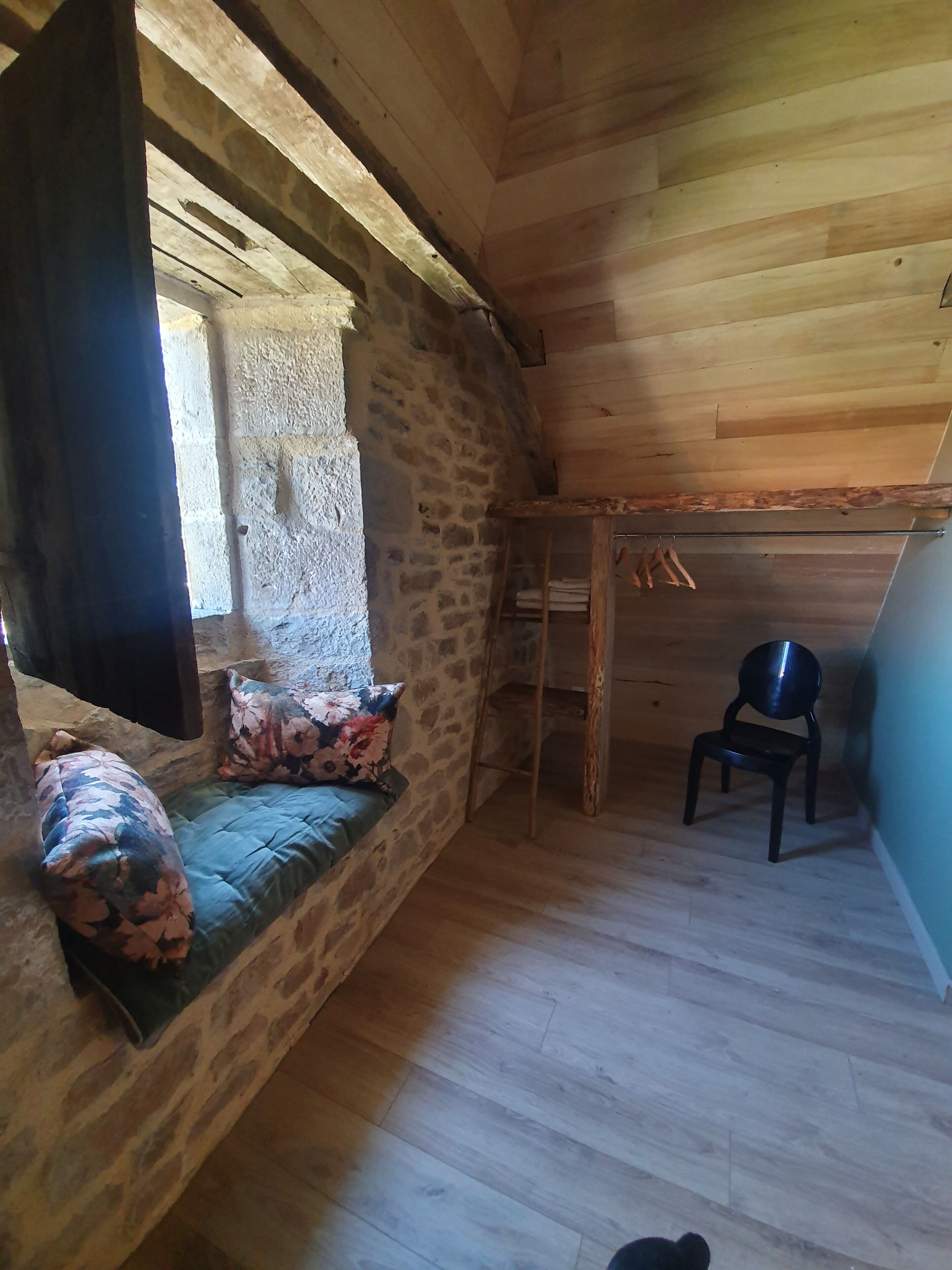 A cozy room with a stone wall, wooden ceiling, and a bench with floral cushions.
