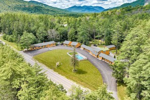 Eine Lodge mit mehreren Holzhütten, einem Schwimmbad und einem Parkplatz, umgeben von dichtem Wald und Bergen.