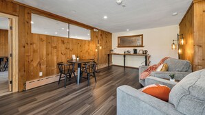 Un interior moderno con paneles de madera, una zona de comedor con una mesa redonda y sillas, y un área de estar con un sofá y sillones.