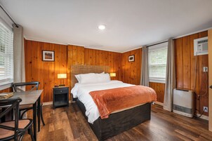 Un dormitorio con cama, mesita de noche, lámpara y ventana con persianas.