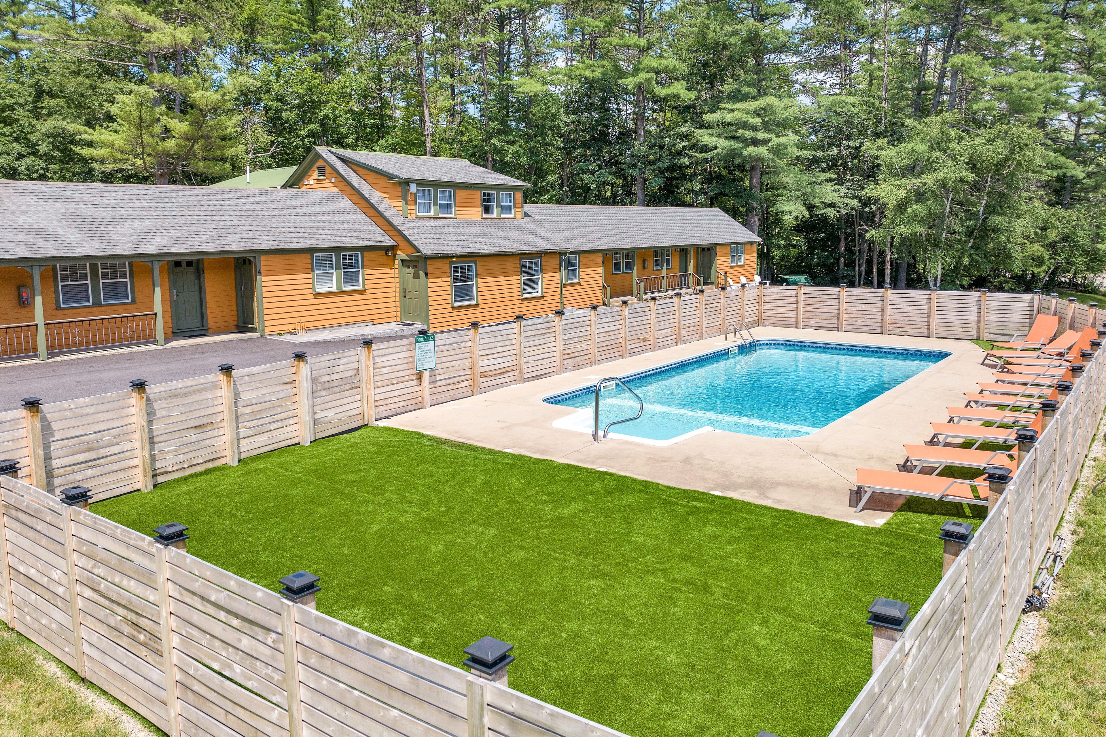 A pool area with a wooden deck, a pool, and lounge chairs.