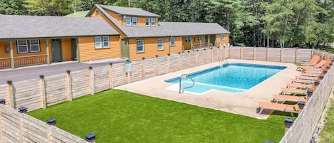 A pool area with a wooden deck, a pool, and lounge chairs.
