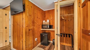 Cocina compacta con paredes de madera, microondas, refrigerador pequeño y un perchero.