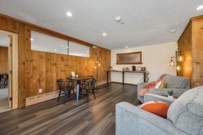 A modern interior with wooden panel walls, a dining area with a round table and chairs, and a seating area with a sofa and armchairs. - The Inn & More (Bartlett)