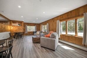 A spacious living area with a sofa, coffee table, and dining table. There are large windows with curtains, a kitchen area, and a visible exit sign. - The Inn & More (Bartlett)