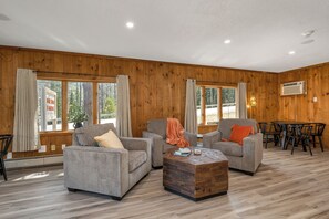 A spacious living room with wooden walls, two grey sofas, a coffee table, and a dining area with a table and chairs. - The Inn & More (Bartlett)