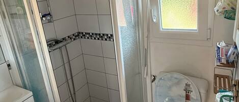 Ein kleines Badezimmer mit Duschkabine, Toilette mit Dekorverkleidung und kleinem Fenster.