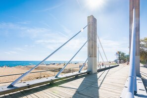 A wooden boardwalk with metal railings, leading to a beach with people and umbrellas. - HomeHolidaysRentals Roure - Costa Barcelona (Calella)