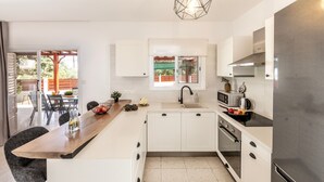 Una cocina moderna con armarios blancos, encimera de madera, refrigerador de acero inoxidable y ventana con vista a un patio.