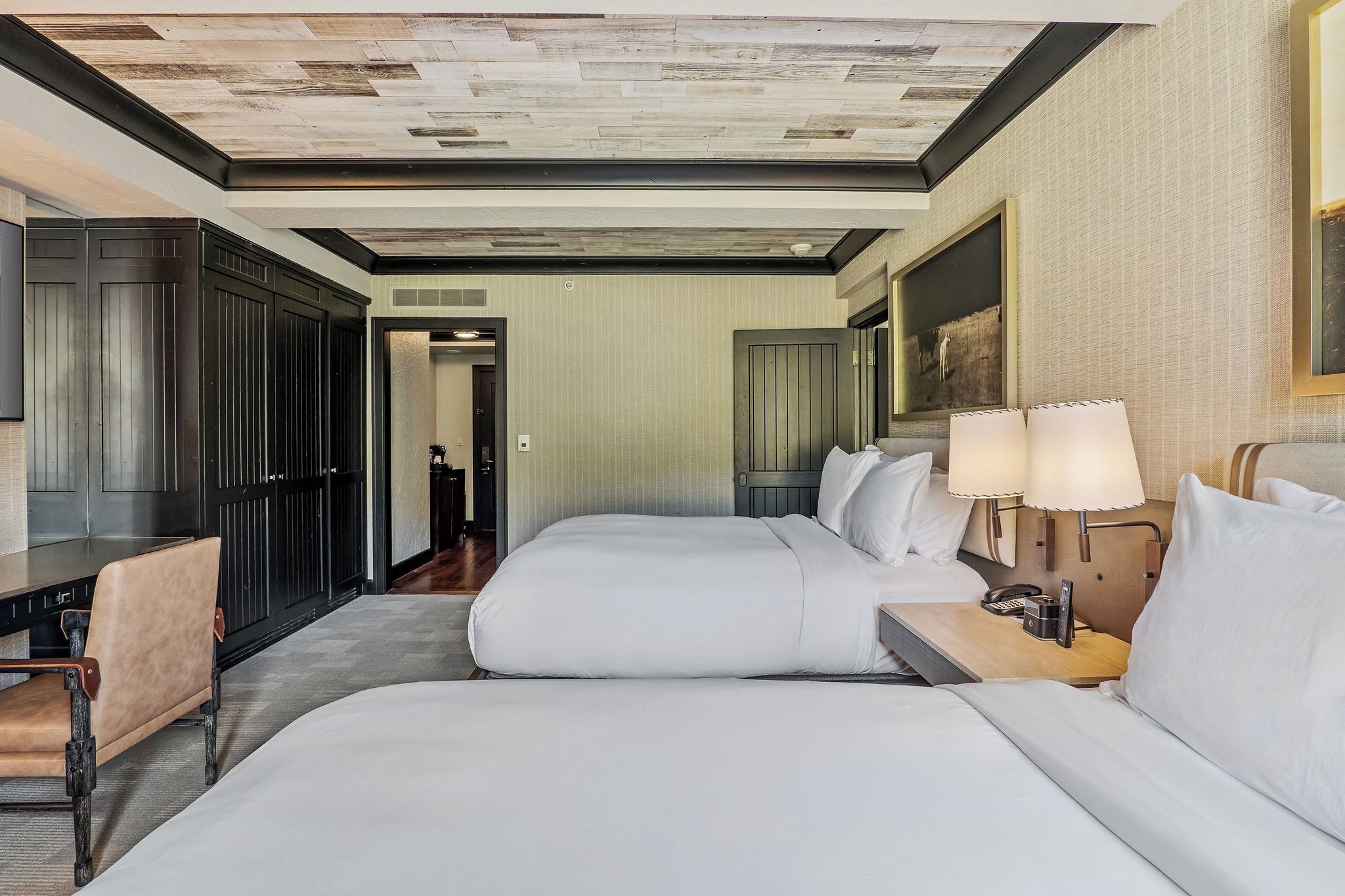 Une chambre d’hôtel avec deux lits, un bureau, une chaise et une lampe.