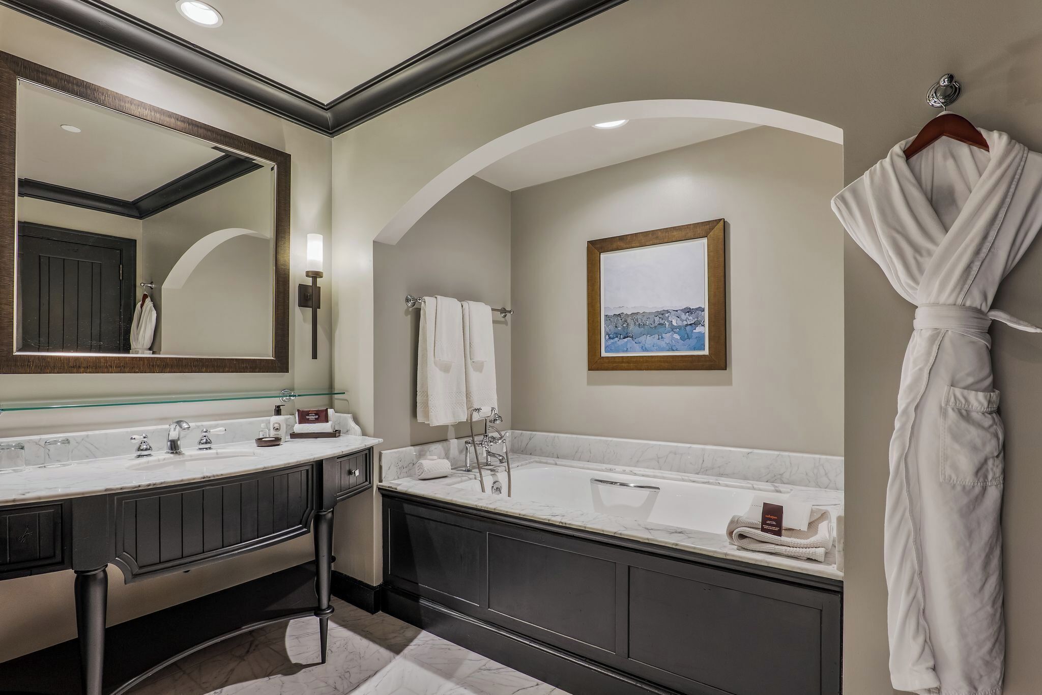 Une salle de bain moderne avec un grand miroir, deux lavabos, une baignoire et un peignoir accroché au mur.