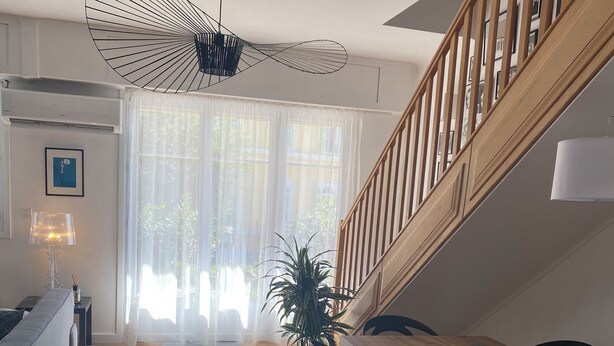 A modern living room with a wooden staircase, a dining table with chairs, a sofa, and a large window with sheer curtains. - Charming duplex apartment in town center (Corte)