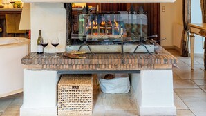 Une cheminée avec un foyer en briques, une cheminée blanche et une porte en verre. On peut voir deux verres à vin et une bouteille sur la cheminée.