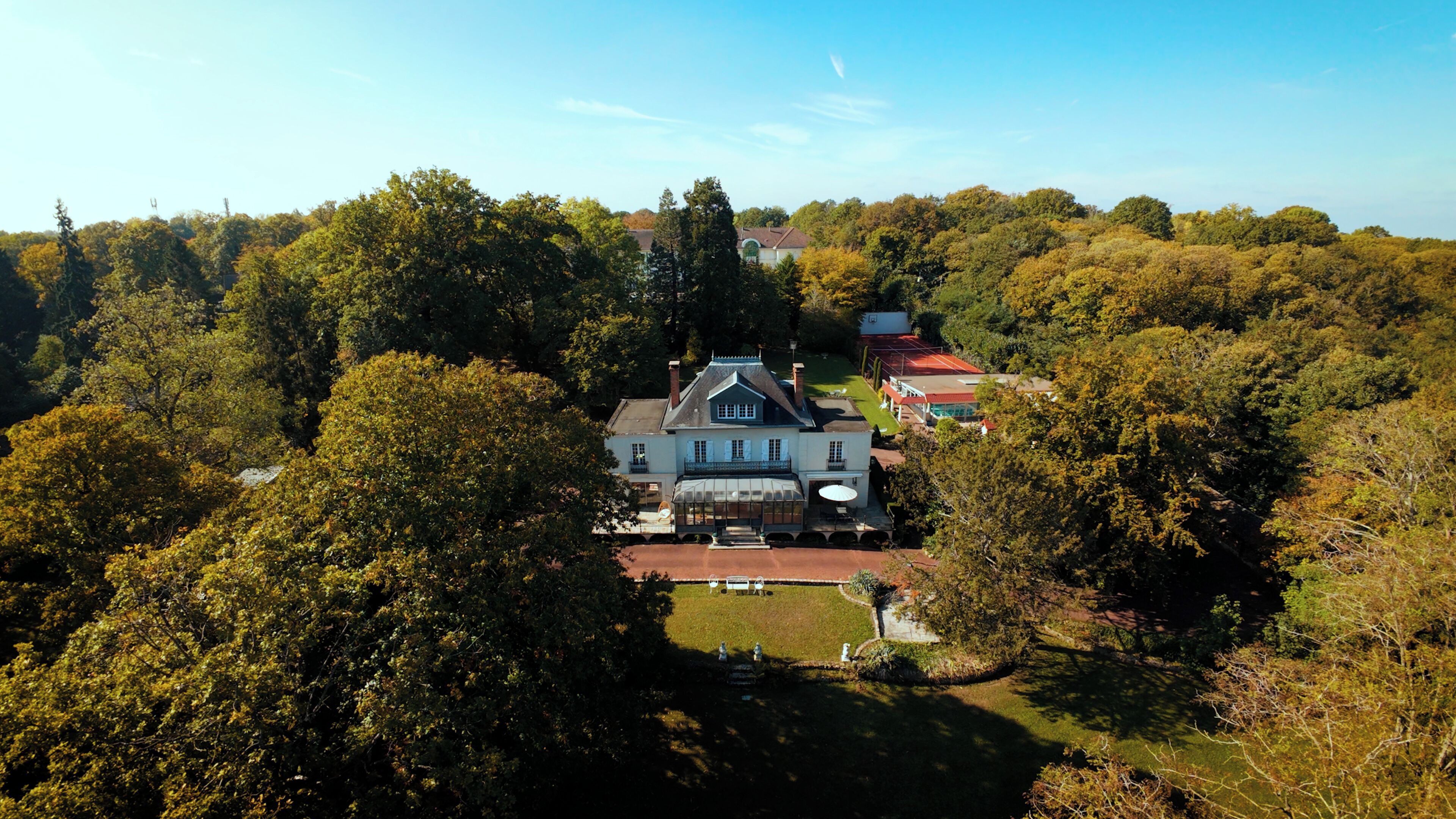 Une grande maison à deux étages, entourée d’une forêt dense.