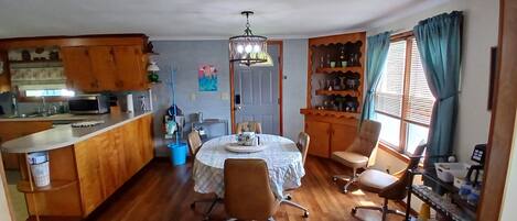 A dining area with a round table, chairs, a chandelier, wooden cabinets, and a window with curtains.