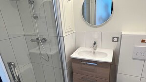 A modern bathroom with a glass-enclosed shower, a white sink with a mirror above it, and a wooden vanity with drawers. - Comfort Studio in a Premium Residence- Sport/cinema (Huningue)